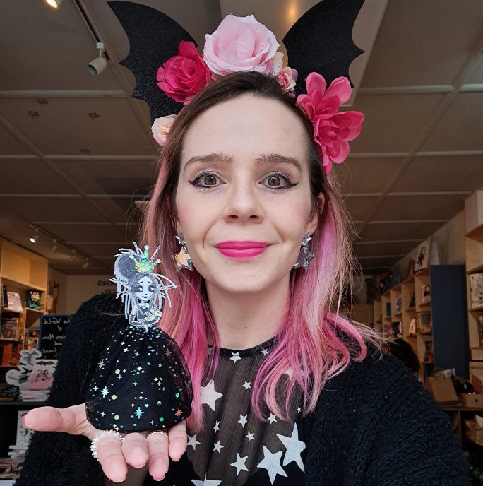 Harriet Muncaster. A woman with pink hair wearing a flower crown, holding a toy